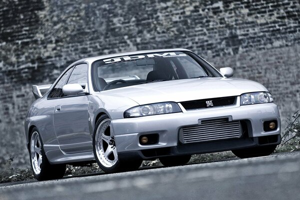 The Nissan car is gray against the background of a brick wall