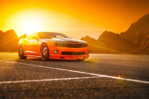 Orange Camaro ss auf dem Hintergrund von Bergen und Sonne