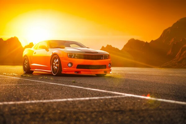 Orange SS Camaro on the background of mountains and the sun