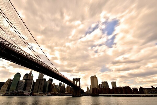 Vue de dessous de la rivière sur le pont de Brooklyn, Manhattan et les nuages