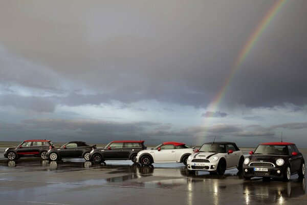 Several mini cooper automobiles on the background of clouds and rainbows after the rain