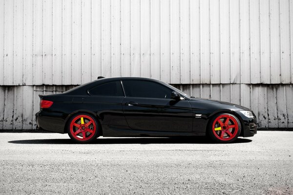 A black BMW with red molding stands on the asphalt