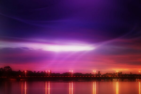 The lights on the bridge are reflected in the water against the background of the lilac sky