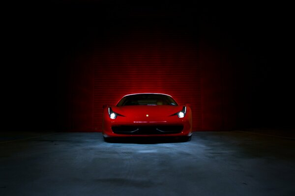 A chic red Ferrari with its headlights on against a concrete wall