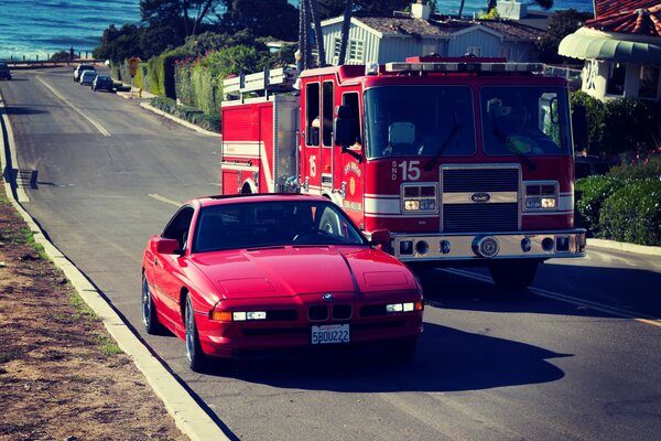 Красный автомобиль BMW едет рядом с пожарной машиной по дороге