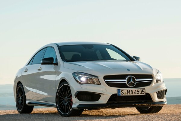 A white Mercedes Benz car is parked on the shore