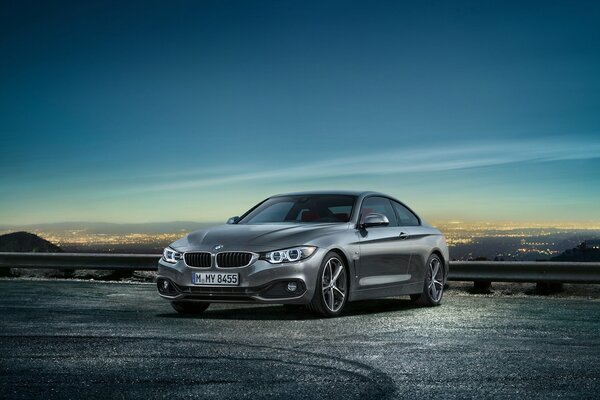 Die vierte Reihe des BMW Coupés in der Nähe des Abstandshalters vor dem Hintergrund einer brennenden Stadt und des Abendhimmels darüber