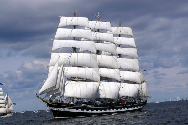 The Cruzenshtern sailing vessel sails on the sea surface against the background of thick bushes growing on thick clouds