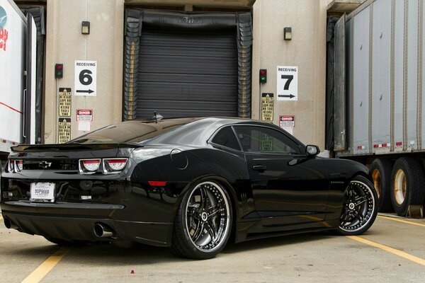 A black car among the warehouse and trucks