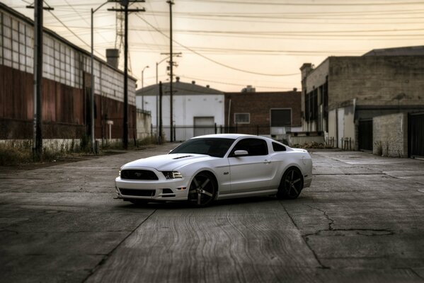 Une Mustang blanche se tient près des maisons abandonnées