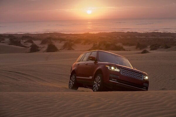 Jeep cavalca attraverso le sabbie al tramonto