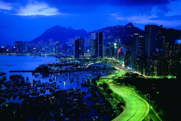 Green road to night skyscrapers and mountains