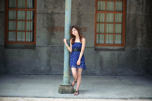 A Japanese woman in a shy pose stands on the street at a pole