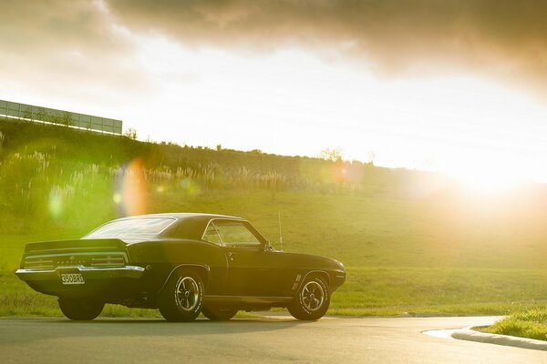 A black pontiac stands on the road against the sunset