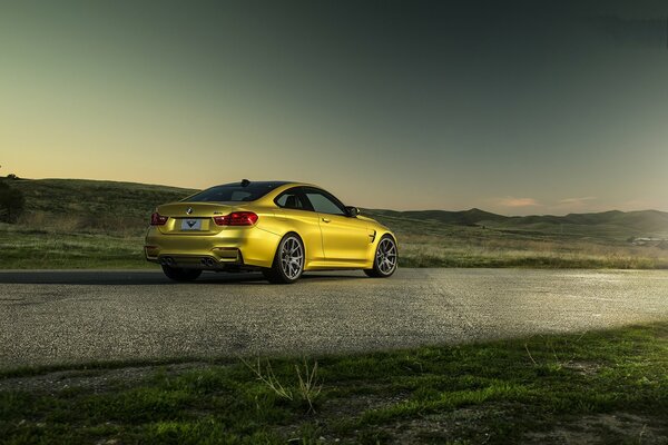 Yellow BMW M4 stands on the road against the background of hills