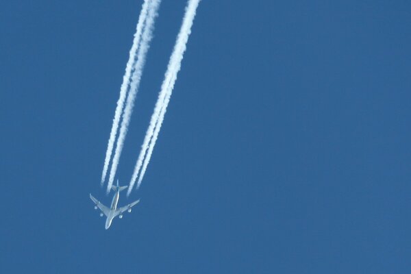 The plane flies in the blue sky leaving a white trail