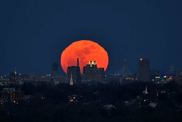 Luces de la ciudad de la noche en el fondo de una enorme Luna roja de sangre