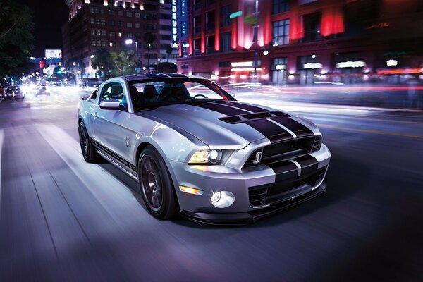 Grey Ford Mustang with two black stripes on the hood against the background of the night city