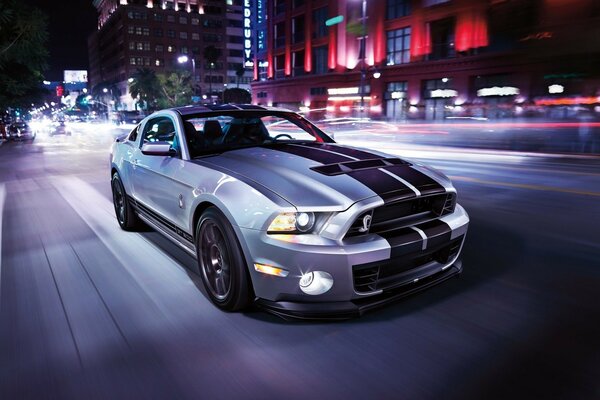 Ford Mustang gris avec deux rayures noires sur le capot sur le fond de la ville de nuit