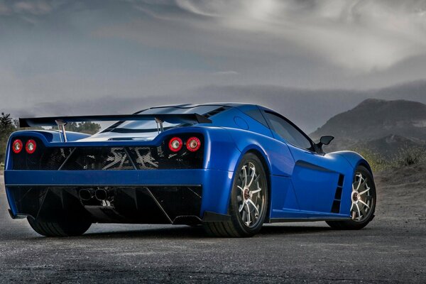 A blue supercar stands on the asphalt against the backdrop of mountains