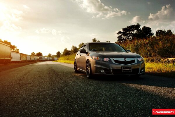 Das Auto des acura tsx ist außerhalb der Stadt. Im Hintergrund fährt ein Güterzug