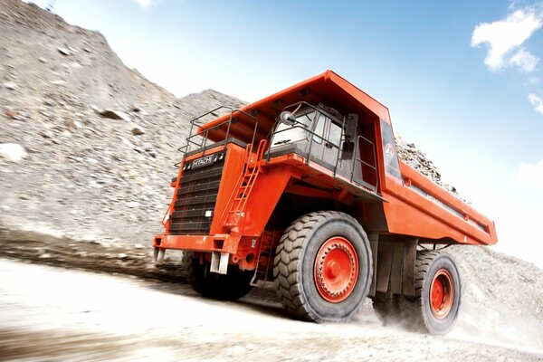 A red dump truck is driving on a sandy gravel road