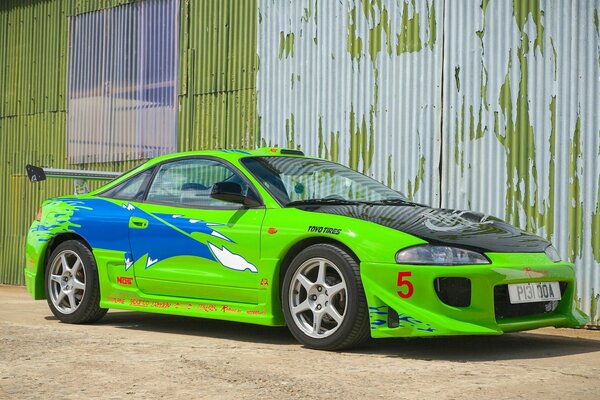 A green car stands against a white-green wall