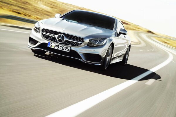 A silver Mercedes is moving along the road