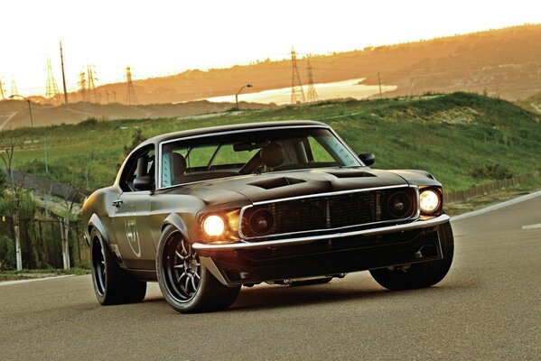 Ford Mustang nera con fari accesi sullo sfondo del tramonto