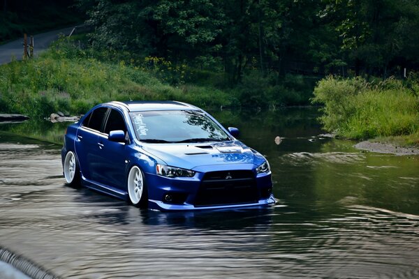 Auto azul marca Mitsubishi Lancer cabalga sobre el agua