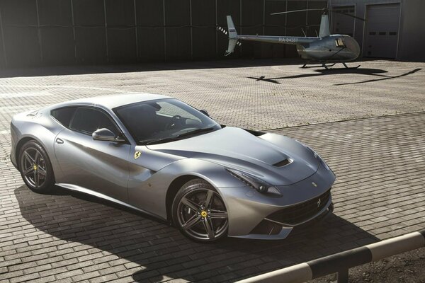 A cute metallic-colored sports supercar parked on the roof next to the helicopter