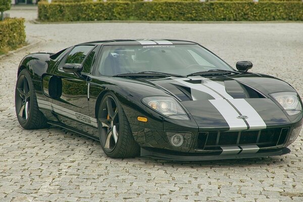 A gray Ford with a stripe in the middle stopped on the cobblestones