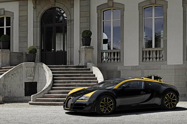 A cool black Bugatti with yellow stripes stopped at a luxurious white mansion