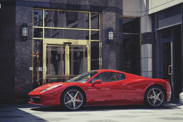 Czerwony sportowy Ferrari przed budynkiem, widok z boku
