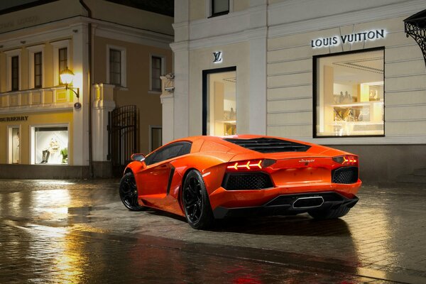 An orange Lamborghini slowed down near a boutique