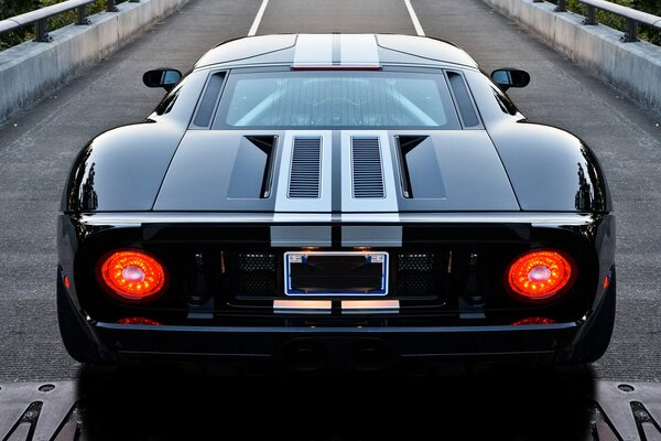 Black sports Ford with rear lights on , rear view