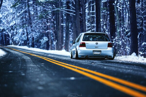 In winter, a volkswagen car is driving along the road in the forest