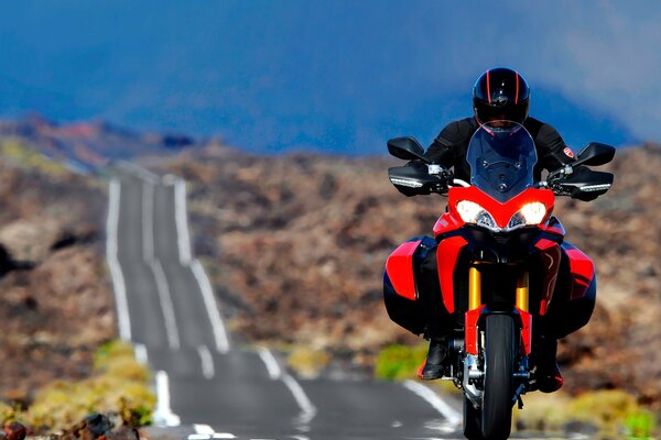 A man is eating on a red ducati on a mountain road