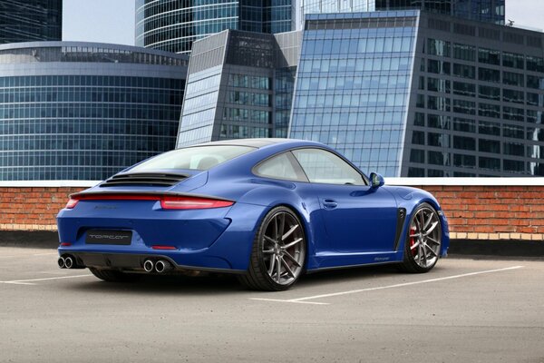 A blue Porshe Carrera 911 Stinger stands on the top floor of a multi-level parking lot