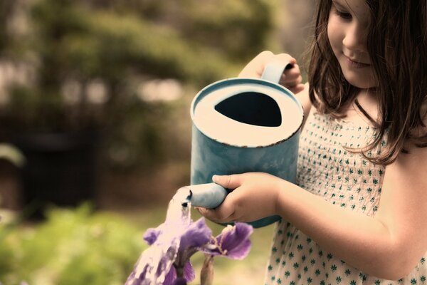 La ragazza innaffia i fiori da un annaffiatoio blu