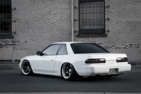 A white Nissan stands against a brick wall