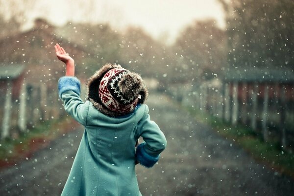 Foto alegre de una niña con un sombrero atrapando los primeros copos de nieve