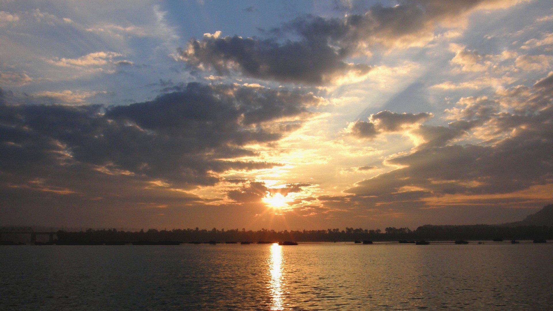 the sun rises grey clouds forest away the reflection of the water water the sky the sun clouds path on the water landscape