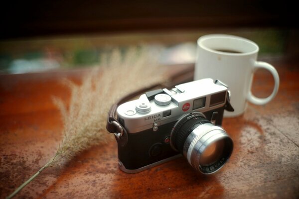 Cámara Leica negra y plateada con un lazo en la mesa con una taza de café