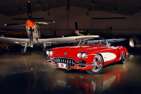 A beautiful red car and an airplane in a hangar