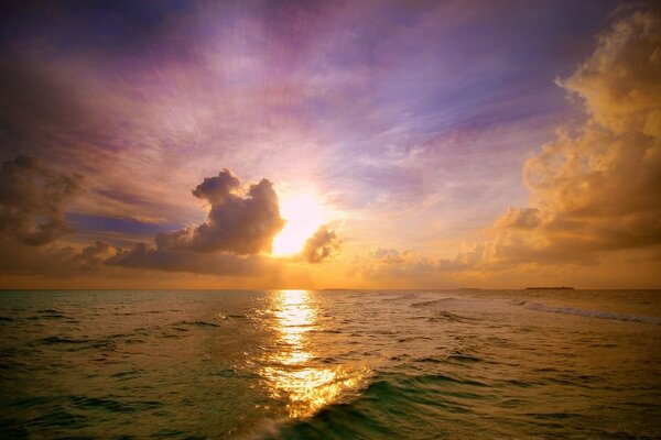 El sol se esconde detrás del horizonte y se refleja en las olas en el agua
