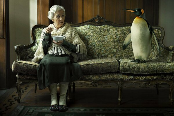 Granny drinks tea with a penguin on her sofa