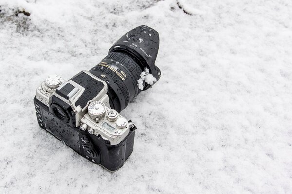 A camera with a large lens lying on the snow