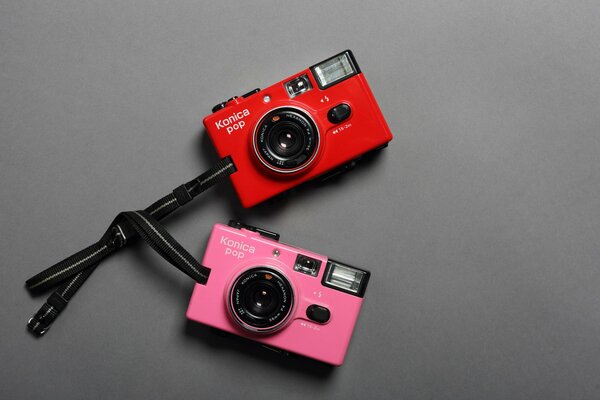 Dos cámaras de color rosa y rojo con lazos sobre un fondo gris