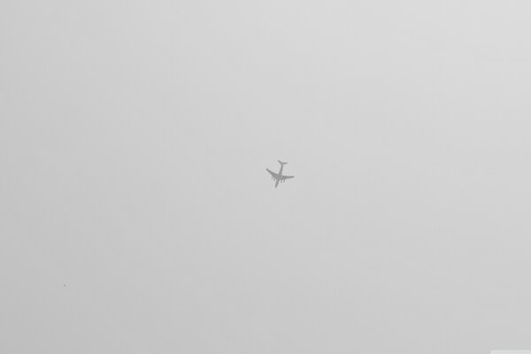 A small plane is flying in the distant gray sky